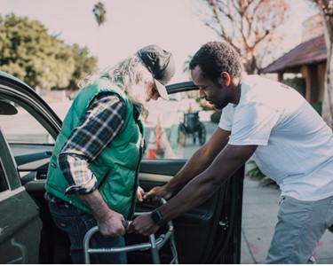 man helping elderly man out of the car with a walker